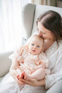 Mutlu genç anne, beş aylıkken kızını kucağında tutuyor. Evdeki bir sandalyede oturuyor..