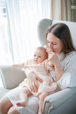 Mutlu genç anne, beş aylıkken kızını kucağında tutuyor. Evdeki bir sandalyede oturuyor..