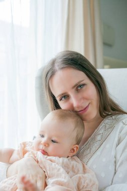 Mutlu genç anne, beş aylıkken kızını kucağında tutuyor. Evdeki bir sandalyede oturuyor..