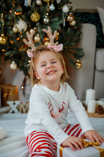 크리스마스 사슴뿔을 머리에 살짜리 스러운 소녀가 크리스마스 근처에서 잠옷을 있습니다 — 스톡 사진