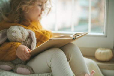 Örgü kazaklı tatlı kıvırcık saçlı bir kız pencerenin önünde kitap okuyor. Rahat bir ev. Ilık sonbahar. Ruh hali.