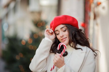 Kış tatili için Avrupa 'da yürüyen kırmızı bereli güzel bir kadının Noel sokak tarzı portresi. Kıvırcık saçlı şık manken yeni yıl alışverişi yapıyor. Samimi.