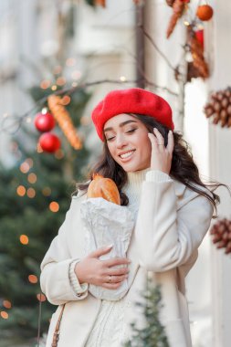 Kış tatili için Avrupa 'da yürüyen kırmızı bereli güzel bir kadının Noel sokak tarzı portresi. Kıvırcık saçlı şık manken yeni yıl alışverişi yapıyor. Samimi.