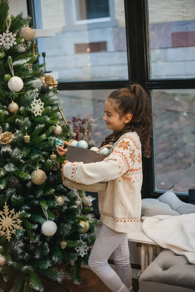 Adorabile bambina dai capelli scuri 9 anni in pigiama vicino all'albero di Natale. Luci di Capodanno. Vacanze invernali. — Foto Stock