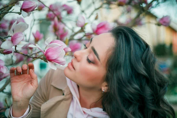Весняний портрет молодої темноволоса кучерявої жінки біля квітучої магнолії. Емоційна модель біля дерева з рожевими квітами. Теплий сезон . — стокове фото