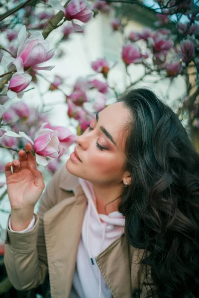 Весняний портрет молодої темноволоса кучерявої жінки біля квітучої магнолії. Емоційна модель біля дерева з рожевими квітами. Теплий сезон . — стокове фото