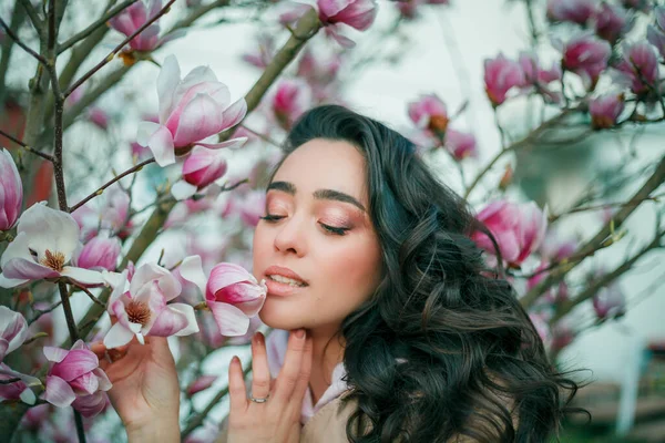 Spring portrait of young dark haired curly woman near blooming magnolia. Emotional model near tree with pink flowers. Warm season. — Stok fotoğraf