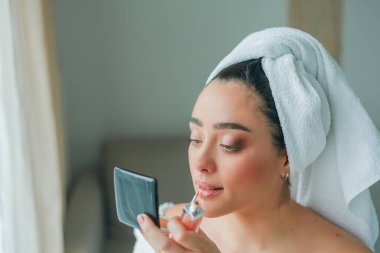Young beautiful woman in terry white dressing gown makes herself beautiful makeup at home. Model holds makeup brush and cosmetics in her hands. Cozy home.