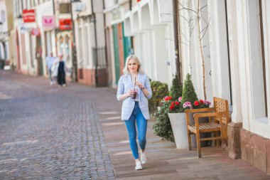 Hafif giysili şık bir sarışın ve elinde bir kokteyl var. Bir Avrupa şehrinin caddesinde güzel, şık bir kadının portresi. Isınma zamanı. Alışverişe. Şehir.