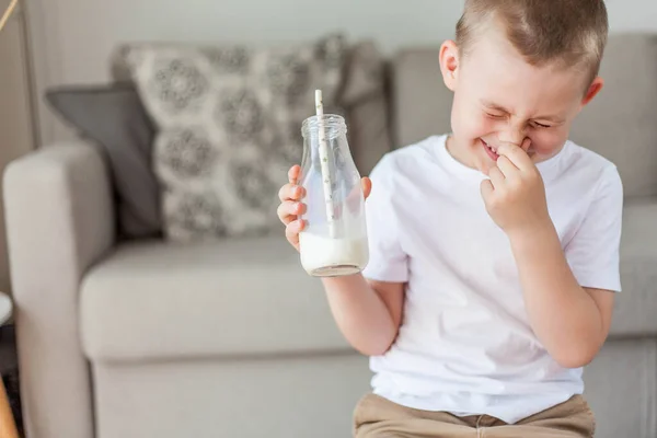 明るい服を着た愛らしい金髪の少年は 自宅で牛乳を飲むことを拒否します エコ製品 健康的な食べ物や飲み物 ミルク — ストック写真