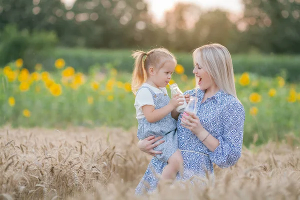 A mãe e a filha adoráveis em vestidos românticos bebem o leite de garrafas de vidro com tubos de papel em um campo de trigo. Retrato de família de verão. Eco. — Fotografia de Stock