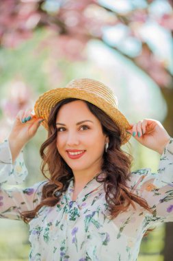 30 yaşında, hasır şapkalı mutlu bir genç kadın lanet olası bir parkta yürüyor. Pembe çiçekli ağaçların yanında açık renk bir elbiseyle şık bir mankenin portresi..