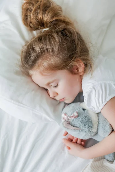 Niña linda con el pelo rizado duerme en la cama en una cama blanca con su juguete de peluche. Un sueño saludable. El niño está descansando.. — Foto de Stock