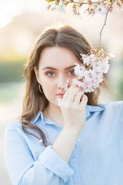 Красива молода жінка 19-річного віку в легкому повсякденному одязі в пастельних відтінках біля квітучих сакури. Весняний портрет моделі з блакитними очима . — стокове фото