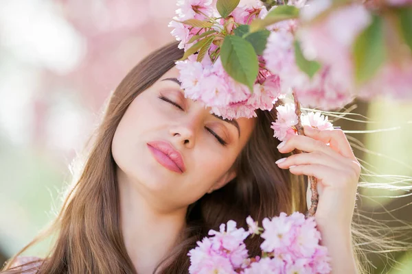 Spring portrait of a young beautiful woman in pink blossoms. Young beautiful model with long hair, in a wicker hat and a light dress near the cherry blossoms. — Stok fotoğraf