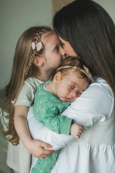 Jovem bela mãe de cabelos escuros em roupas leves com suas filhas em uma casa aconchegante. Irmãzinhas. Raparigas. Família. Mãe feliz. — Fotografia de Stock