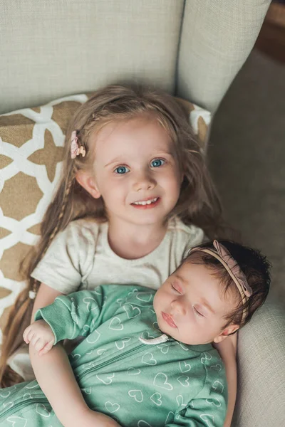Older 4-year-old sister holds her little newborn sister in her arms in a cozy house. Family. — Stock fotografie