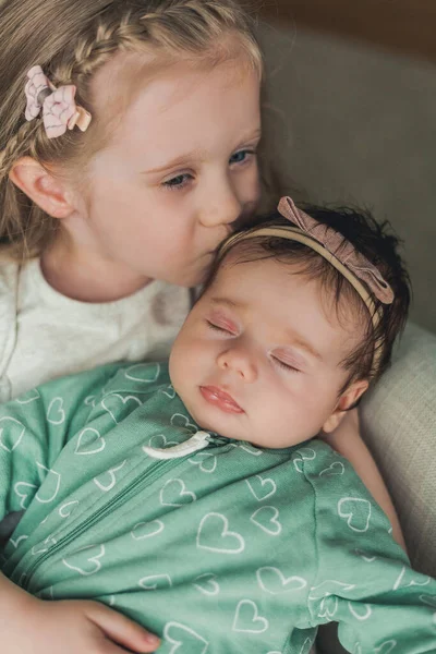 A irmã mais velha de 4 anos segura sua irmãzinha recém-nascida em seus braços em uma casa aconchegante. Família. — Fotografia de Stock