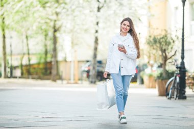 Uzun saçlı, rahat, gündelik kıyafetleri olan, bluetooth kulaklık takan, Avrupa 'nın merkezinde yürüyen güzel bir kadın. Şirin bir model alışveriş yapıyor..