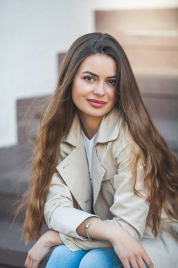 Portrait of a young beautiful long-haired woman in a European city. A model in stylish casual wear is relaxing outside. Spring.