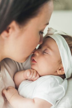Genç bir annenin kollarında beyaz takım elbiseli, tatlı, siyah saçlı, yeni doğmuş bir kızın yakın portresi. Annelik. Ebeveyn. İyi uykular. Ev.