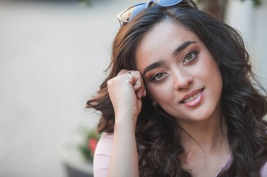 Genç, kıvırcık, siyah saçlı, mutlu bir kadının yaz portresi. Bir Avrupa şehrinin sokaklarında günlük giysiler içinde. Modelin güneşli portresi. Sokak hayatı. Yaz.