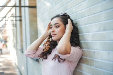 Genç, kıvırcık, siyah saçlı, mutlu bir kadının yaz portresi. Bir Avrupa şehrinin sokaklarında günlük giysiler içinde. Modelin güneşli portresi. Sokak hayatı. Yaz.