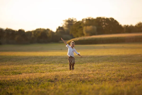5 yaşında, açık renk elbiseli, sevimli, sarışın bir çocuk gün batımında güneşin altında koşuyor. Mutlu çocuk. Yaz akşamı..