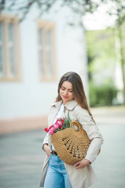 28 yaşında, uzun, bakımlı saçlarıyla genç ve güzel bir kadının bahar portresi elinde bir şehir caddesinde bir buket lale ile bir hasır çanta tutuyor. Tarz modeli