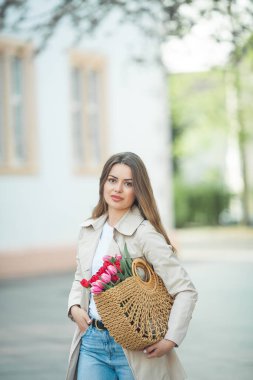 28 yaşında, uzun, bakımlı saçlarıyla genç ve güzel bir kadının bahar portresi elinde bir şehir caddesinde bir buket lale ile bir hasır çanta tutuyor. Tarz modeli
