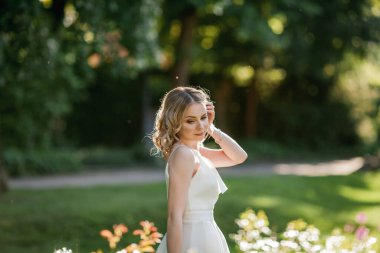 Parktaki güneşli günbatımı ışınlarında beyaz elbiseli, kıvırcık saçlı, genç, güzel, 20 'li yaşlarda bir sarışın. Şık bir model yazın lanet olası parklarda dolaşıyor. Yaz.