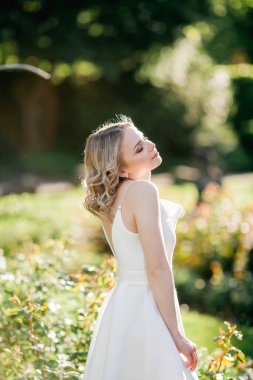 Parktaki güneşli günbatımı ışınlarında beyaz elbiseli, kıvırcık saçlı, genç, güzel, 20 'li yaşlarda bir sarışın. Şık bir model yazın lanet olası parklarda dolaşıyor. Yaz.