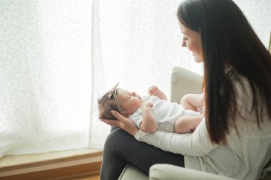 Genç bir annenin kollarında beyaz takım elbiseli, tatlı, siyah saçlı, yeni doğmuş bir kızın yakın portresi. Annelik. Ebeveyn. İyi uykular. Ev.