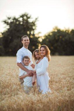 Beautiful young family at sunset in a wheat field. Happy parents with two children, a boy and a girl, in light clothes. Summer. Love.