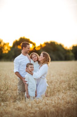 Beautiful young family at sunset in a wheat field. Happy parents with two children, a boy and a girl, in light clothes. Summer. Love.