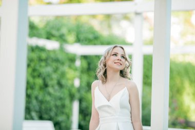 Parktaki güneşli günbatımı ışınlarında beyaz elbiseli, kıvırcık saçlı, genç, güzel, 20 'li yaşlarda bir sarışın. Şık bir model yazın şehrin lanet parkında yürüyor. Yaz.