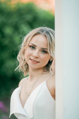 Parktaki güneşli günbatımı ışınlarında beyaz elbiseli, kıvırcık saçlı, genç, güzel, 20 'li yaşlarda bir sarışın. Şık bir model yazın şehrin lanet parkında yürüyor. Yaz.