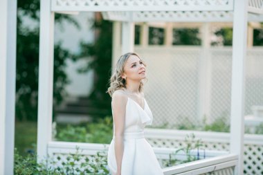 Parktaki güneşli günbatımı ışınlarında beyaz elbiseli, kıvırcık saçlı, genç, güzel, 20 'li yaşlarda bir sarışın. Şık bir model yazın şehrin lanet parkında yürüyor. Yaz.