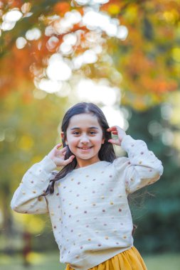Portrait of a little beautiful girl of 9 years old with long dark hair in bright clothes. Happy child in autumn park. Fall.