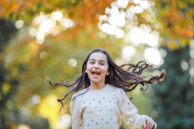 Portrait of a little beautiful girl of 9 years old with long dark hair in bright clothes. Happy child in autumn park. Fall.