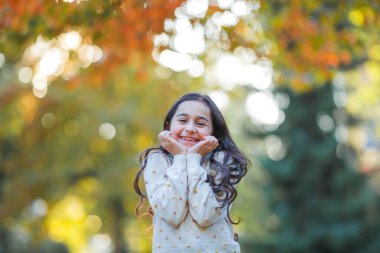 Portrait of a little beautiful girl of 9 years old with long dark hair in bright clothes. Happy child in autumn park. Fall.