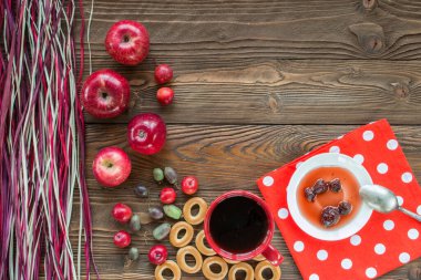 Kırmızı çay, olgun kırmızı elmalar, aktinidia üzümleri, simit, beyaz çay tabağında çilek reçeli, kaşık, ahşap masadaki beyaz polka noktalarında kırmızı peçete ve dekoratif renkli kuru pipet. en üstteki görünüm