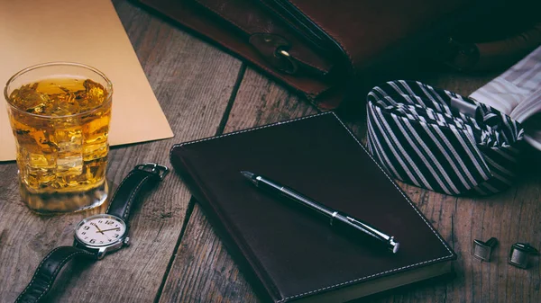 İş aksesuarları - defter, kalem, zengin portföy, saat, kravat, ahşap zemin üzerinde buz olan bir bardak viski