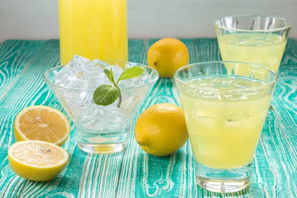 limonata ya da limonata bardakta buz küpleriyle şerbet bardağı, nane yaprağıyla süslenmiş buz bardağı, turkuaz renkli ahşap masa üzerinde limon meyveleri beyaz benekli sarı peçete