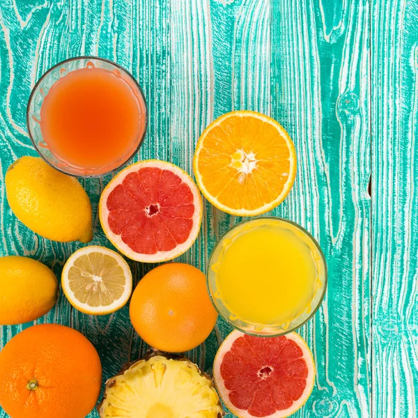 fresh juice from citrus fruits - lemon, grapefruit, orange, pine apple in glasses on  turquoise colored wooden background, top view. copy space, free space for your text.