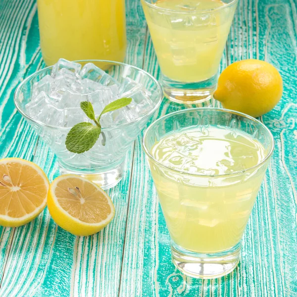 limonata ya da limonata bardakta buz küpleriyle şerbet bardağı, nane yaprağıyla süslenmiş buz bardağı, turkuaz renkli ahşap masa üzerinde limon meyveleri beyaz benekli sarı peçete
