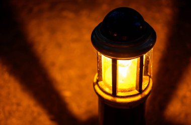 Gece lamba ya da ışık dairesel desenli gölgeli bir parkta. Işık taşlı bir yolu aydınlatıyor. Lambanın, ampulü ve örümcek ağını gösteren yakın görüntüsü. Arkaplan bulanık.