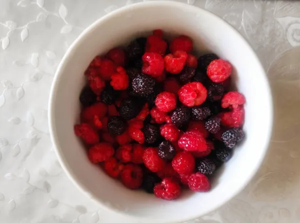 Kırmızı ve siyah böğürtlenler masa örtüsünün üzerinde beyaz bir kasede.