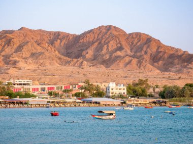 Akabe, Ürdün - 09.01.2021: Günbatımında Akabe plajı ile manzara. Açık masalar, sandalyeler ve sahildeki tekneler..