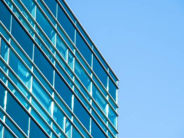 Açık mavi gökyüzüne karşı modern cam ofis binası.